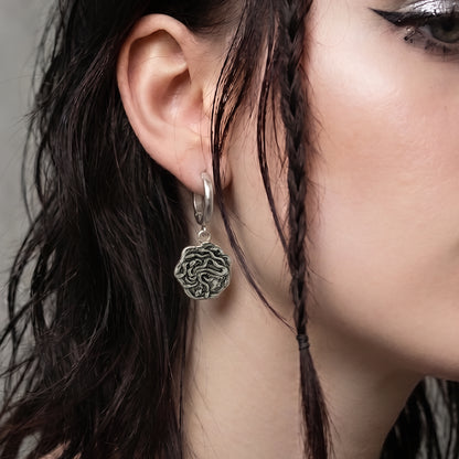 model wearing petrifying gaze dangle earrings in silver, featuring a medusa-inspired charm suspended from a hoop