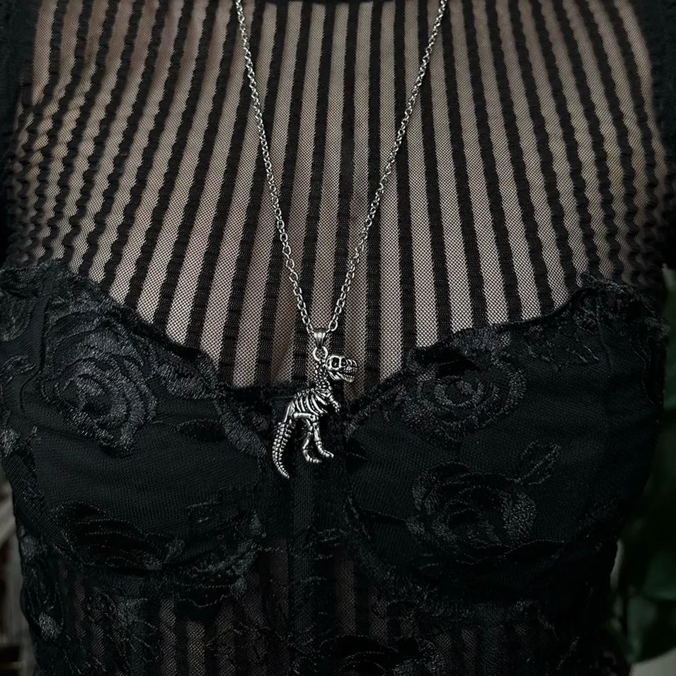 Close-up of a silver-tone dinosaur skeleton pendant on a chain, resting on a black lace and mesh top