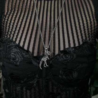Close-up of a silver-tone dinosaur skeleton pendant on a chain, resting on a black lace and mesh top