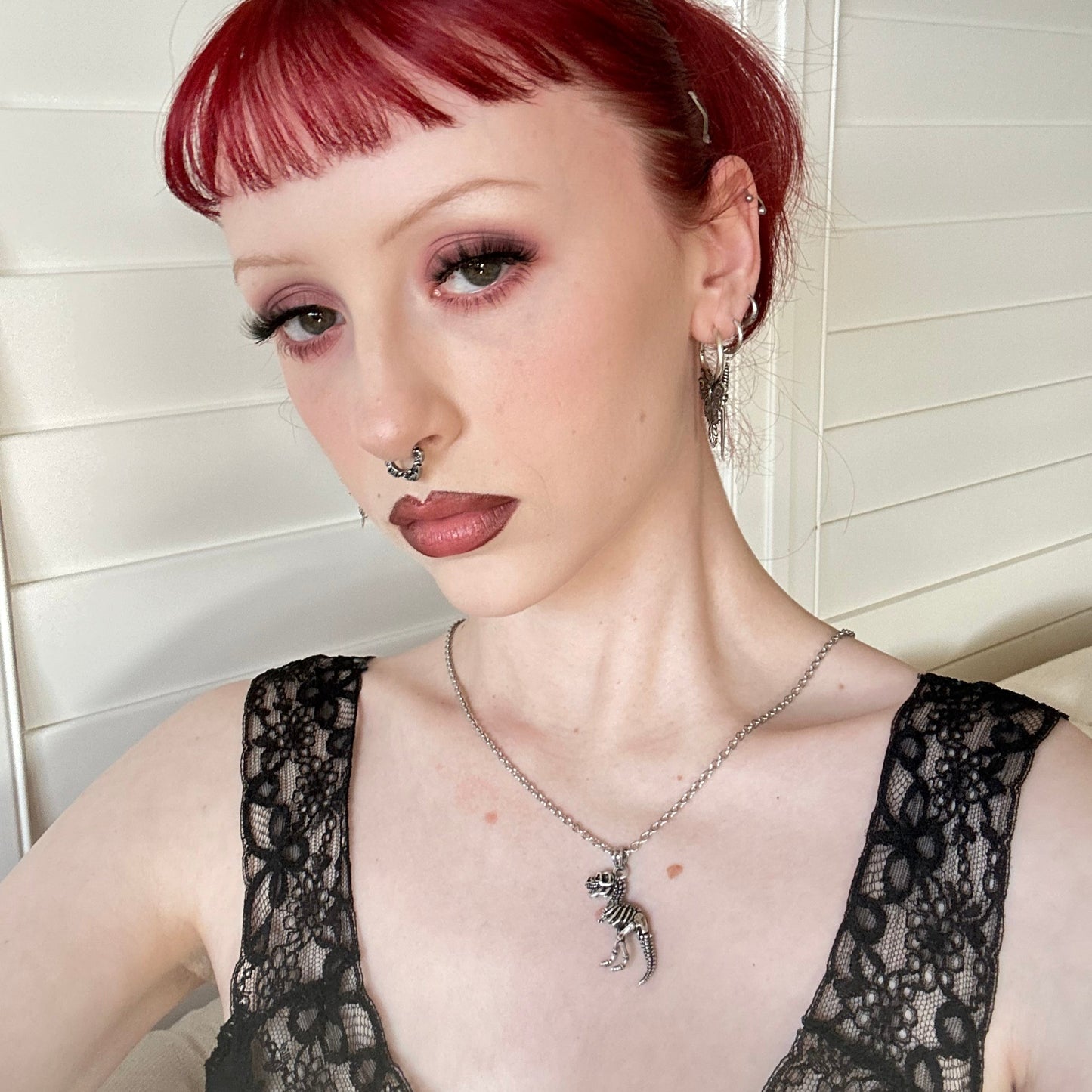Model with red hair wearing a silver-tone dinosaur skeleton pendant necklace over a black lace top