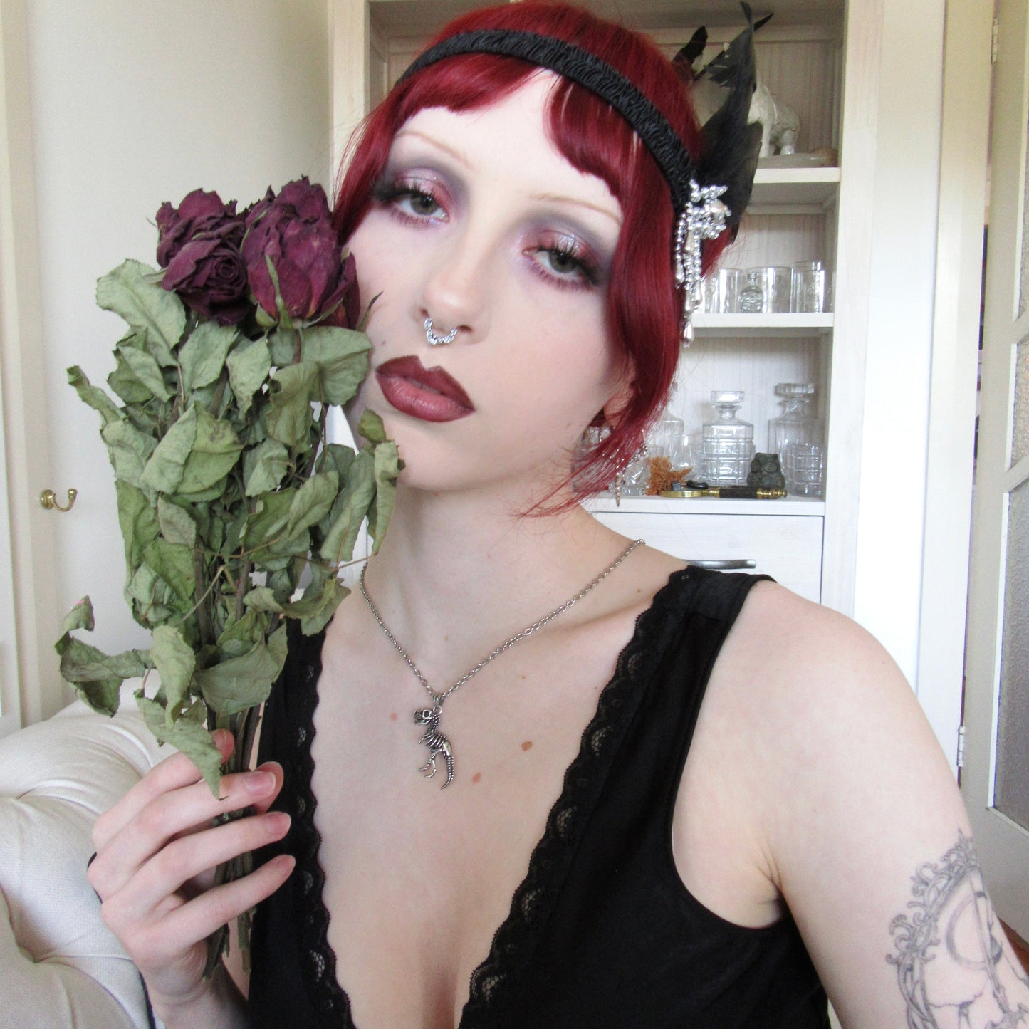 Model in a black dress holding dried roses while wearing a silver-tone T-rex skeleton pendant necklace