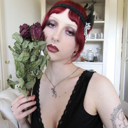 Model in a black dress holding dried roses while wearing a silver-tone T-rex skeleton pendant necklace