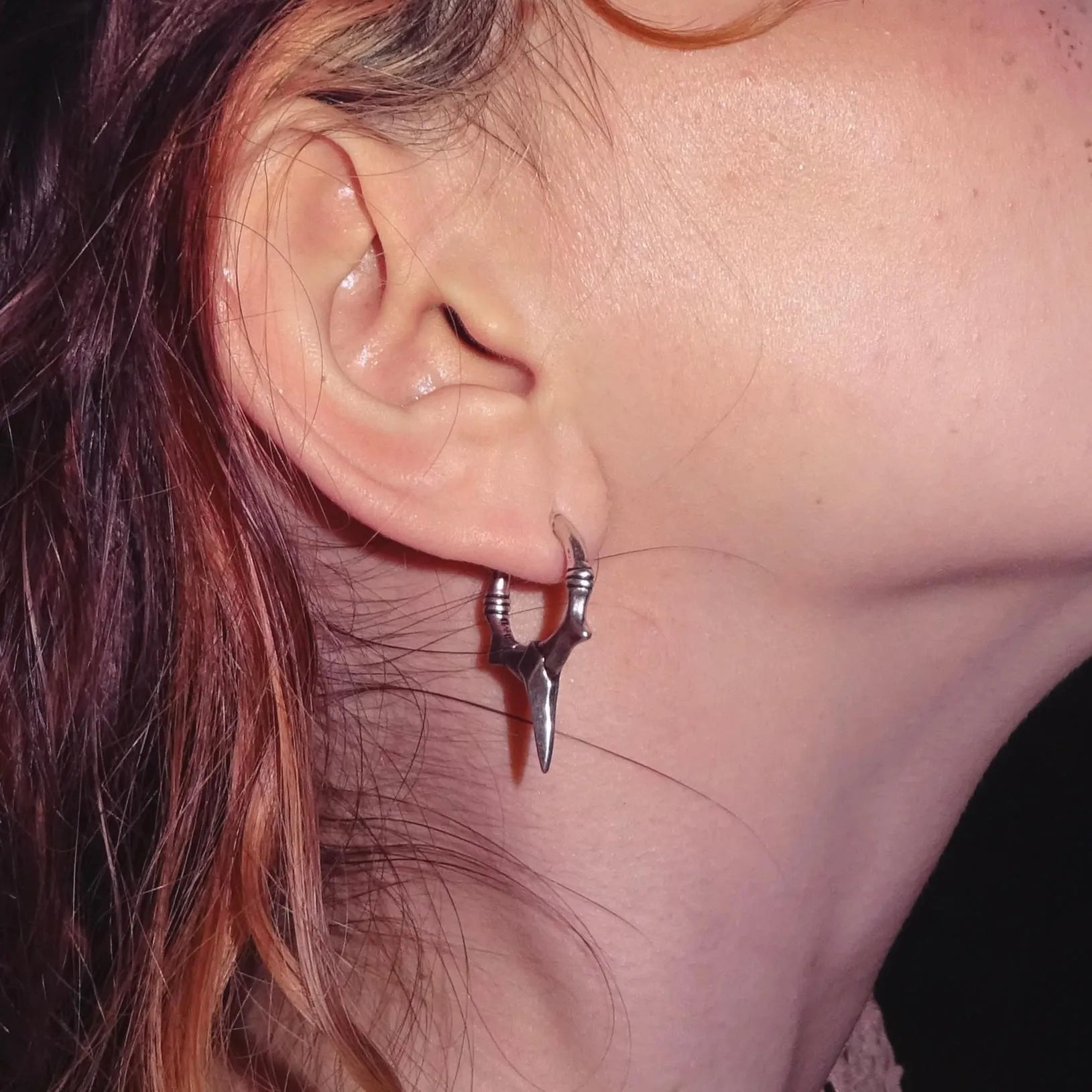 Close-up of an ear wearing a unique silver earring with a dark background