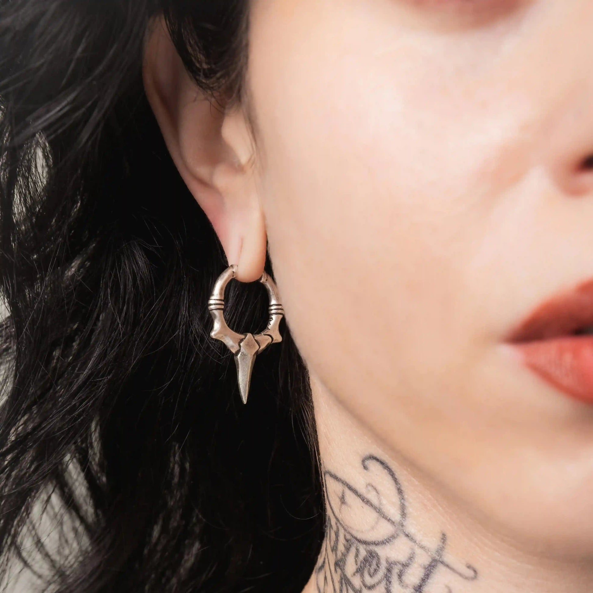 Model wearing silver Primal Blade Earrings with dagger-shaped hoop design and antiqued brass finish
