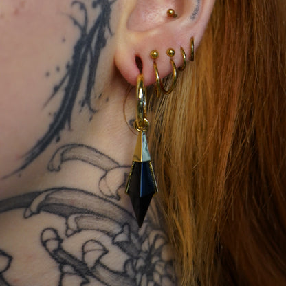 Model wearing the gold Prism Apex Earrings with black crystal drops, polished hoops, and bold geometric styling.