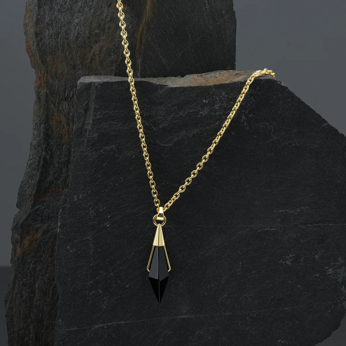 Gold-tone Prism Apex Necklace with a black crystal pendant displayed against a dark stone backdrop.