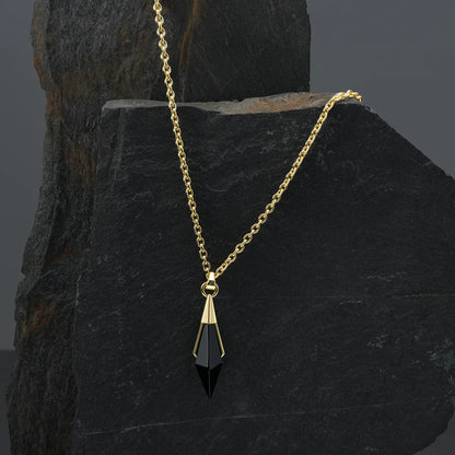 Gold-tone Prism Apex Necklace with a black crystal pendant displayed against a dark stone backdrop.
