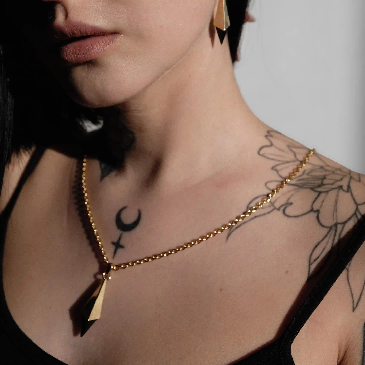 Angled close-up of the gold-tone Prism Apex Necklace worn with a faceted black crystal pendant.