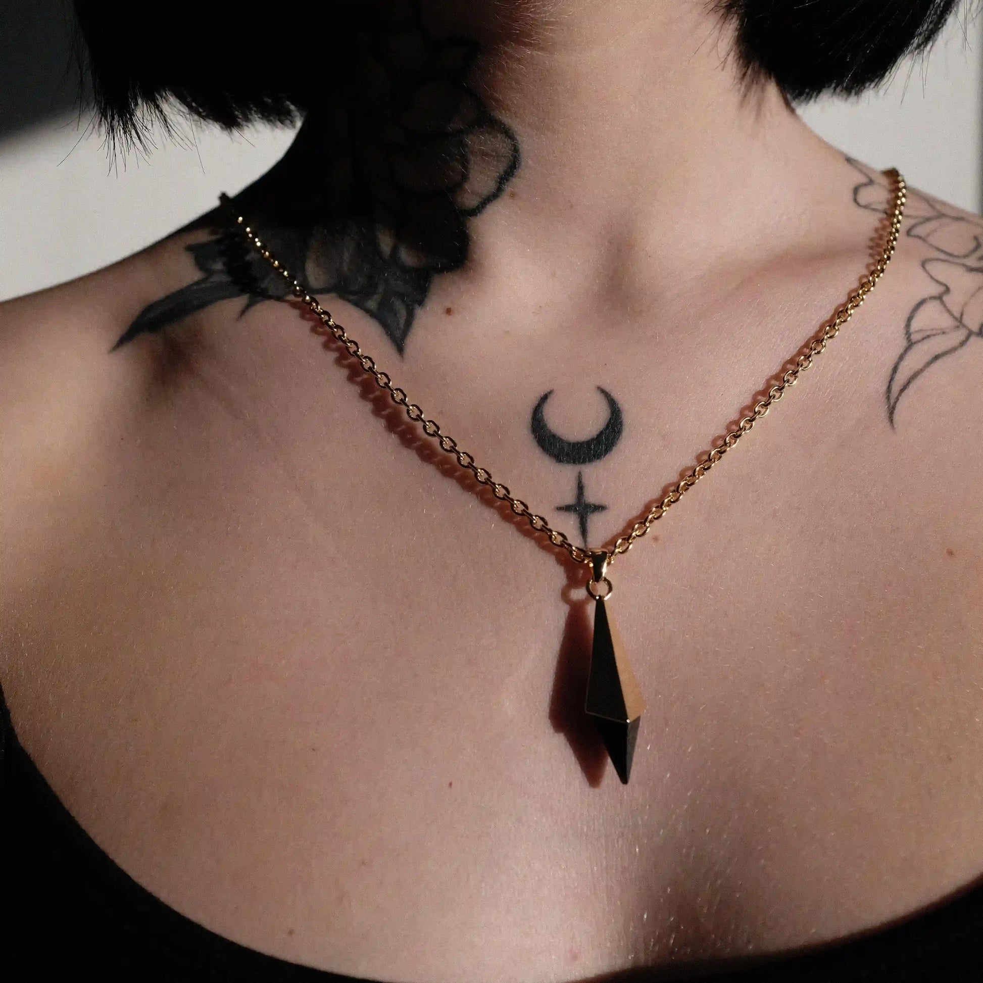 Gold-tone Prism Apex Necklace worn at the center of the chest with a pointed black crystal pendant.