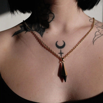 Gold-tone Prism Apex Necklace worn at the center of the chest with a pointed black crystal pendant.