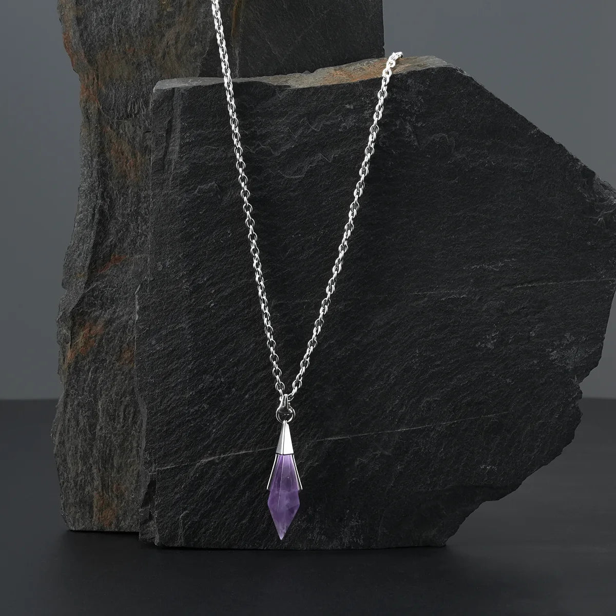 Silver-tone Prism Apex Necklace with a purple crystal pendant displayed against a dark stone backdrop.