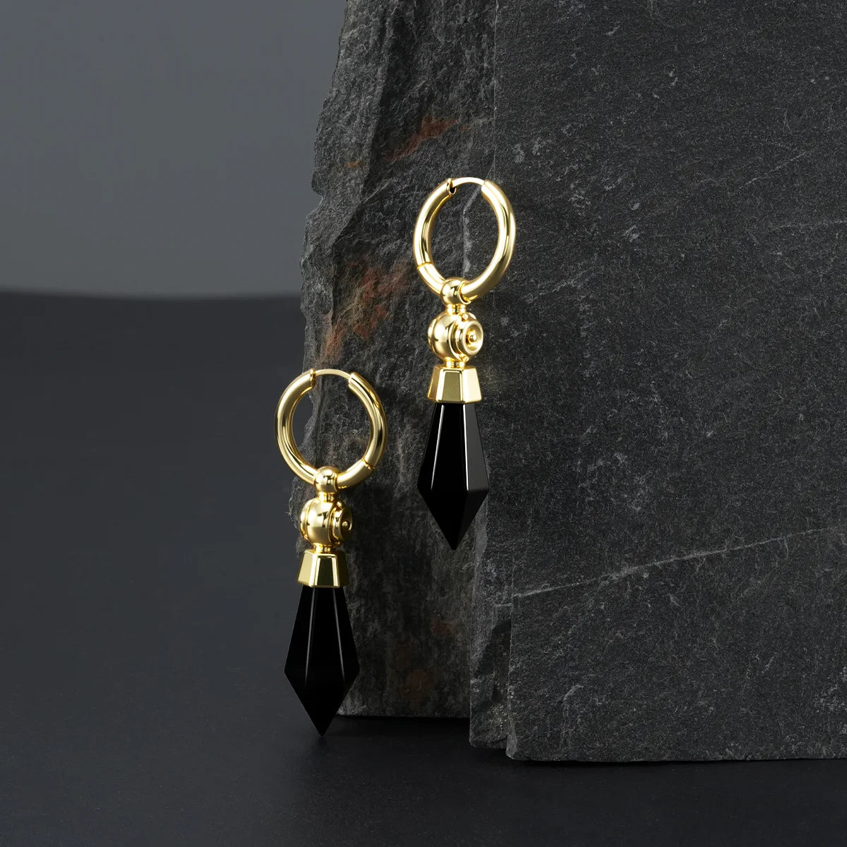 Gold Prism Orb Earrings displayed on a dark stone surface, highlighting the black crystal drops, orb beads, and polished hoop design.