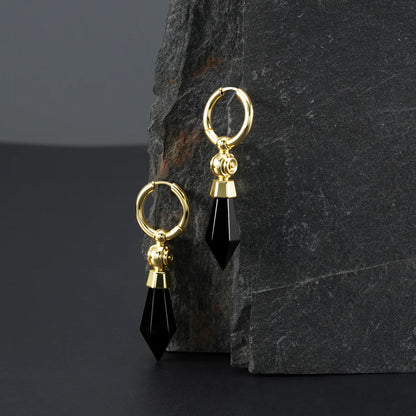Gold Prism Orb Earrings displayed on a dark stone surface, highlighting the black crystal drops, orb beads, and polished hoop design.