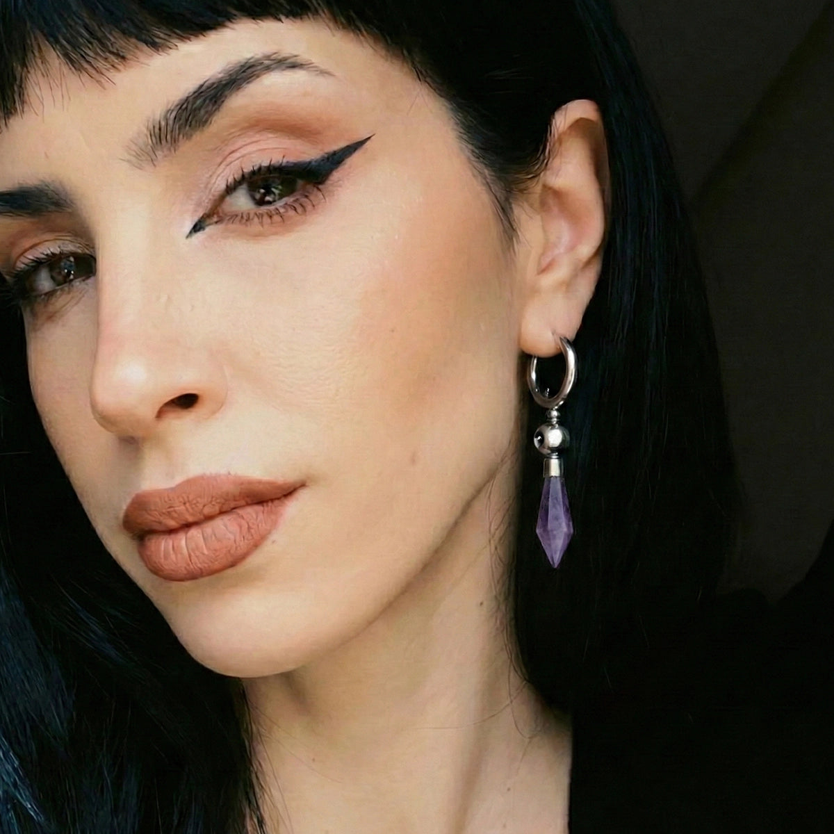 Model wearing the silver Prism Orb Earrings with amethyst crystal drops, spherical bead details, and dark geometric styling.