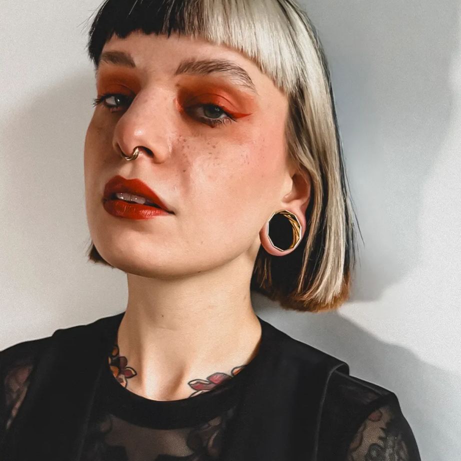 Model with short bob haircut wearing a black and gold-tone faceted tunnel earring and a nose ring