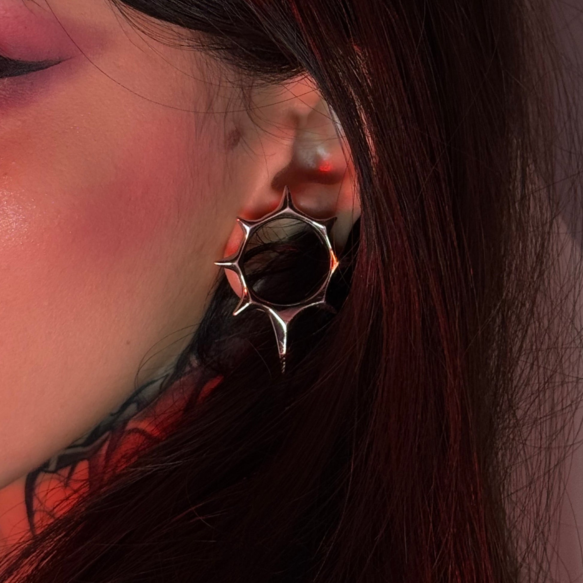 Close-up of a silver-tone star tunnel earring worn in the ear lobe with dark hair background