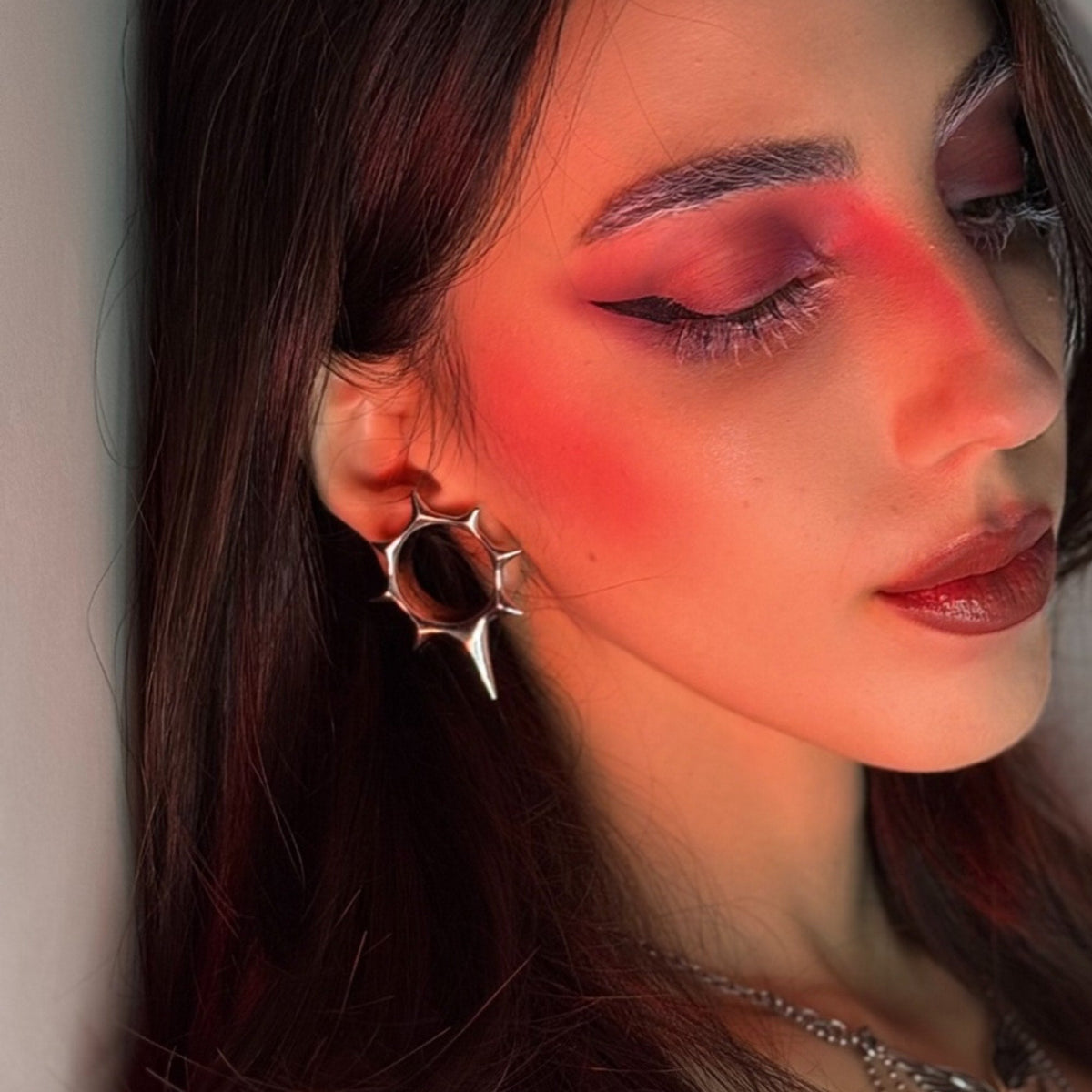 Model wearing a silver-tone star-shaped tunnel earring with red-toned makeup and dark hair