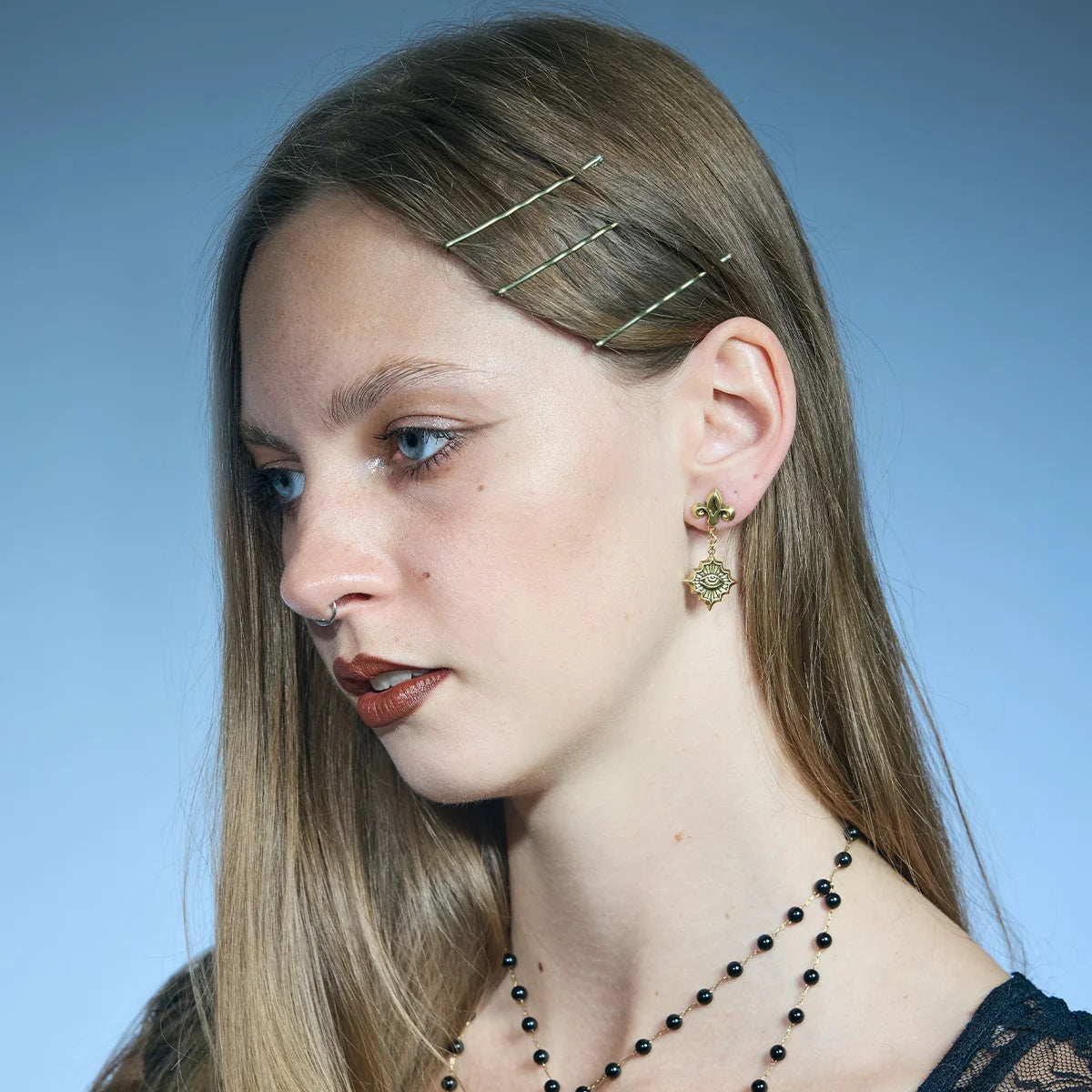 Gold-tone Radiant Witness Drop Earrings worn in a downward-looking portrait, highlighting the suspended radiant eye medallions.