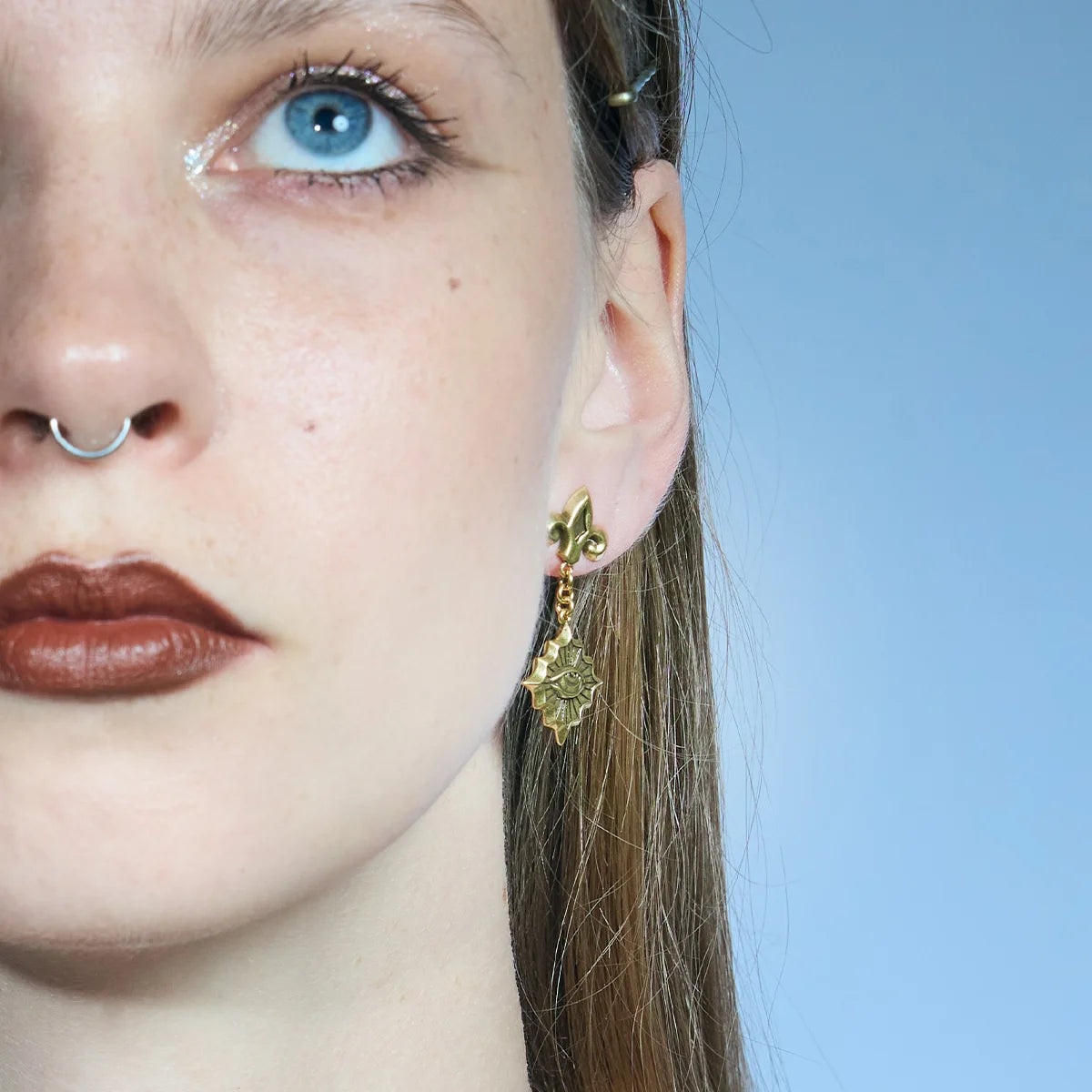 Front close-up of a gold-tone Radiant Witness Drop Earring with a sculpted eye motif and pointed radiating frame.