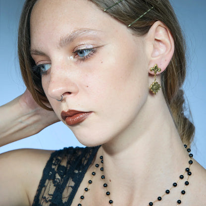Gold-tone Radiant Witness Drop Earrings worn in a styled portrait, featuring sculpted eye medallions and radiating pointed frames.