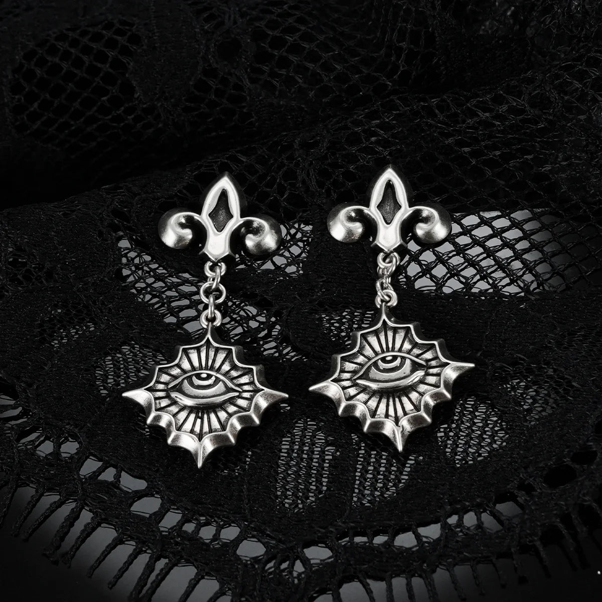 Antiqued silver-tone Radiant Witness Drop Earrings displayed as a pair against black lace on a dark reflective surface.