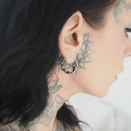 Silver-tone twisted hoop earring worn by a model with dark hair and visible neck tattoos, close side view