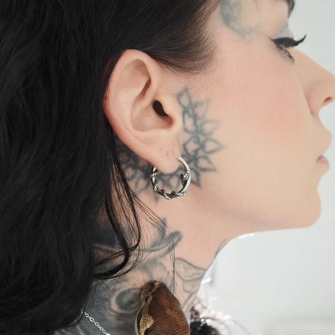 Twisted silver-tone hoop earring shown on a model's ear with a star tattoo on the cheek, profile angle