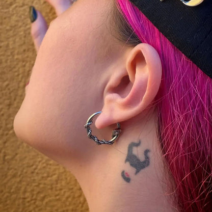 Thorn-style silver-tone hoop earring worn by a model with pink hair and a small neck tattoo