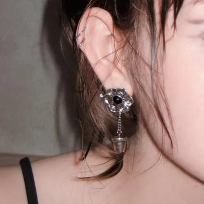 Model wearing the silver Relic Bloom Ear Studs with black obsidian flower center, suspended vessel charm, and gothic relic styling.