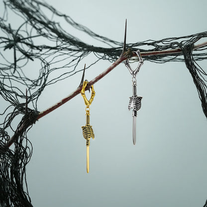 Silver and gold Ribcage Blade earrings hanging from a dark branch