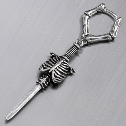Close-up of a silver-tone bone hoop earring with ribcage and blade charm on textured surface