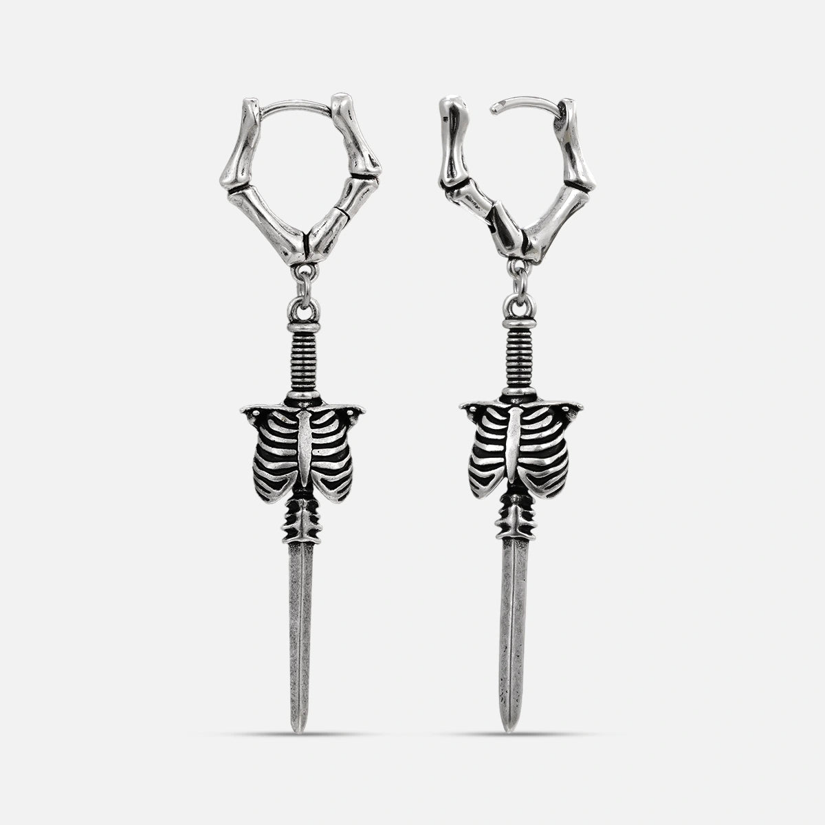 Silver-tone bone hoop earrings with dangling ribcage and blade charms on white background
