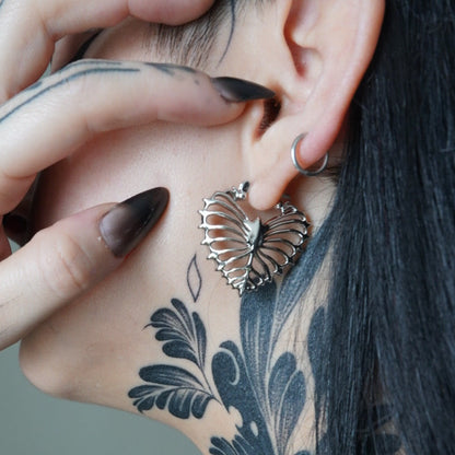 Ribheart earring worn on tattooed neck and ear, close-up view of heart-shaped rib cage design