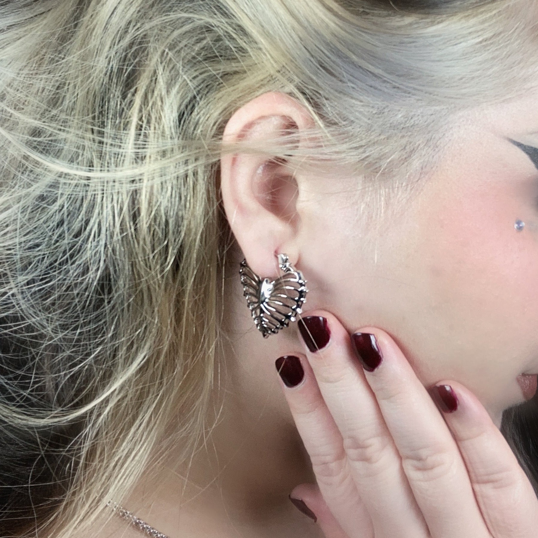 Small ribheart earring worn on blonde model, close-up view of heart-shaped rib cage motif in earlobe