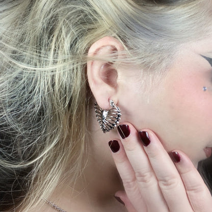 Small ribheart earring worn on blonde model, close-up view of heart-shaped rib cage motif in earlobe