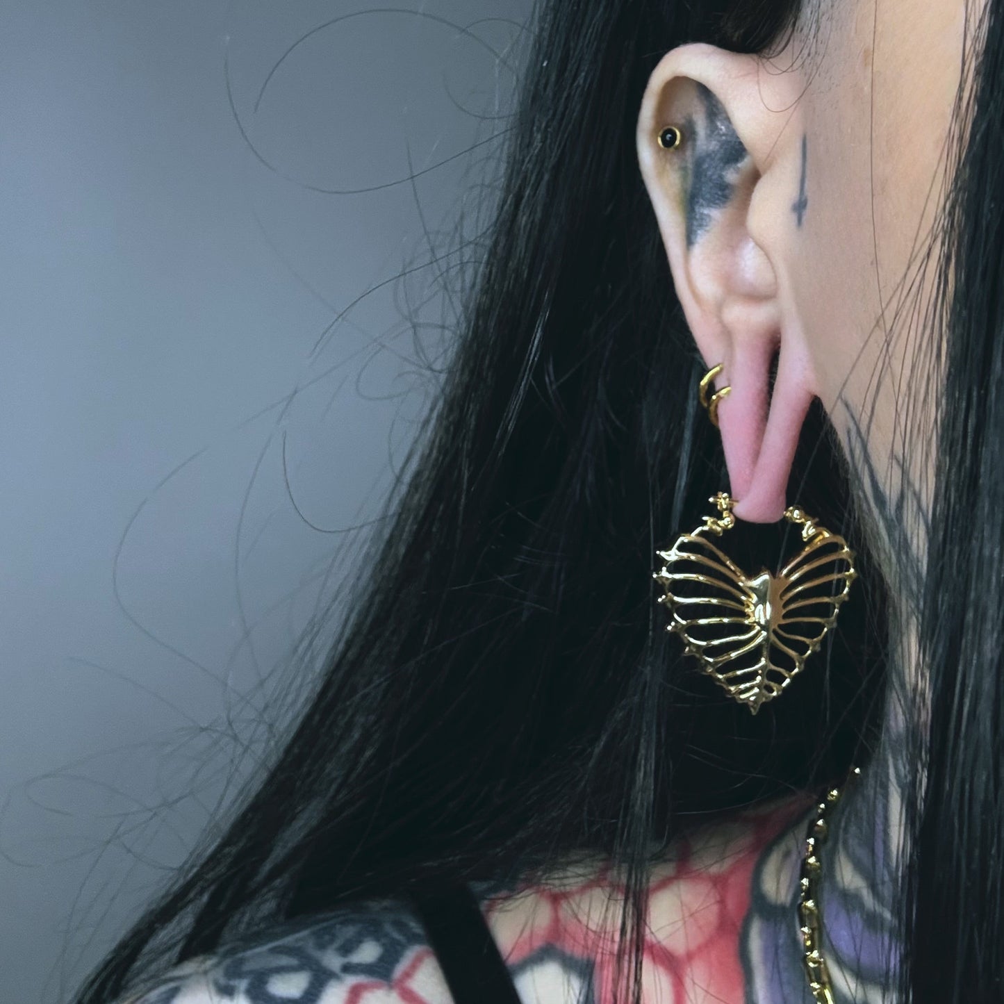 Gold Ribheart earring hanging below a pink ear plug