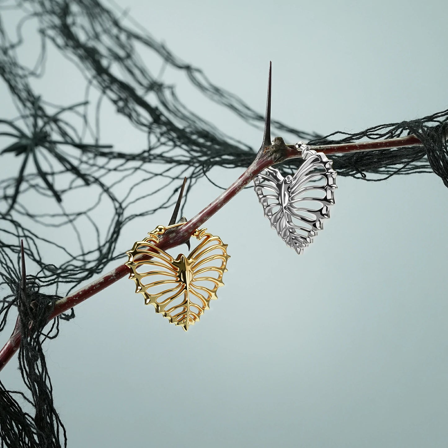 Silver and gold Ribheart earrings hanging from a dark branch
