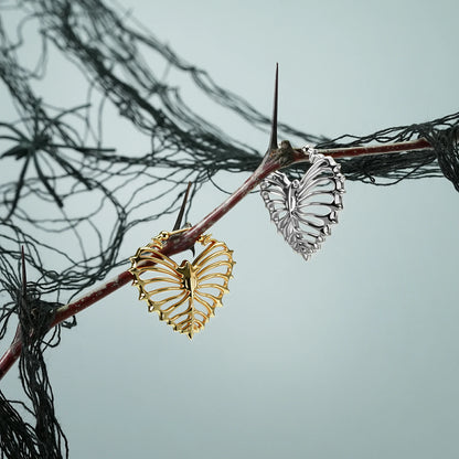 Silver and gold Ribheart earrings hanging from a dark branch