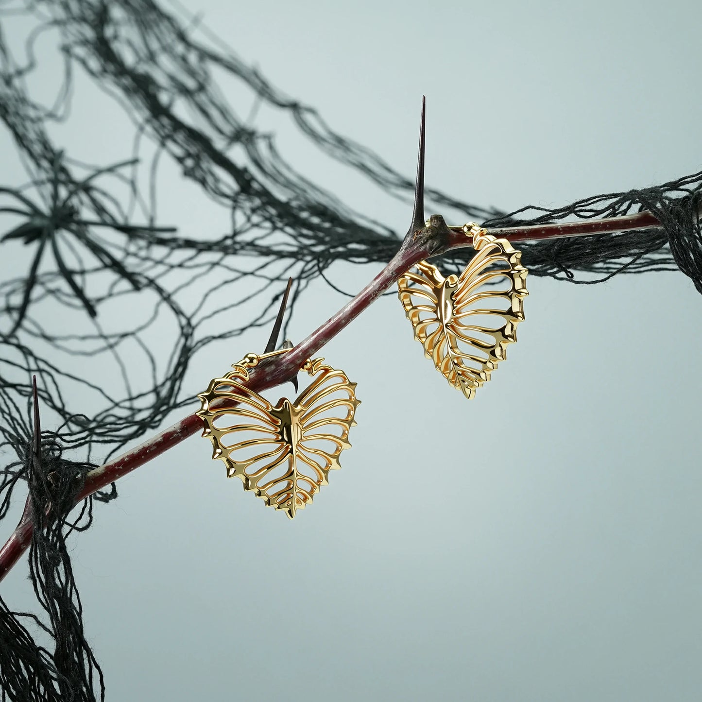 Pair of gold Ribheart earrings hanging from a dark branch