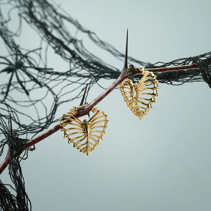 Pair of gold Ribheart earrings hanging from a dark branch