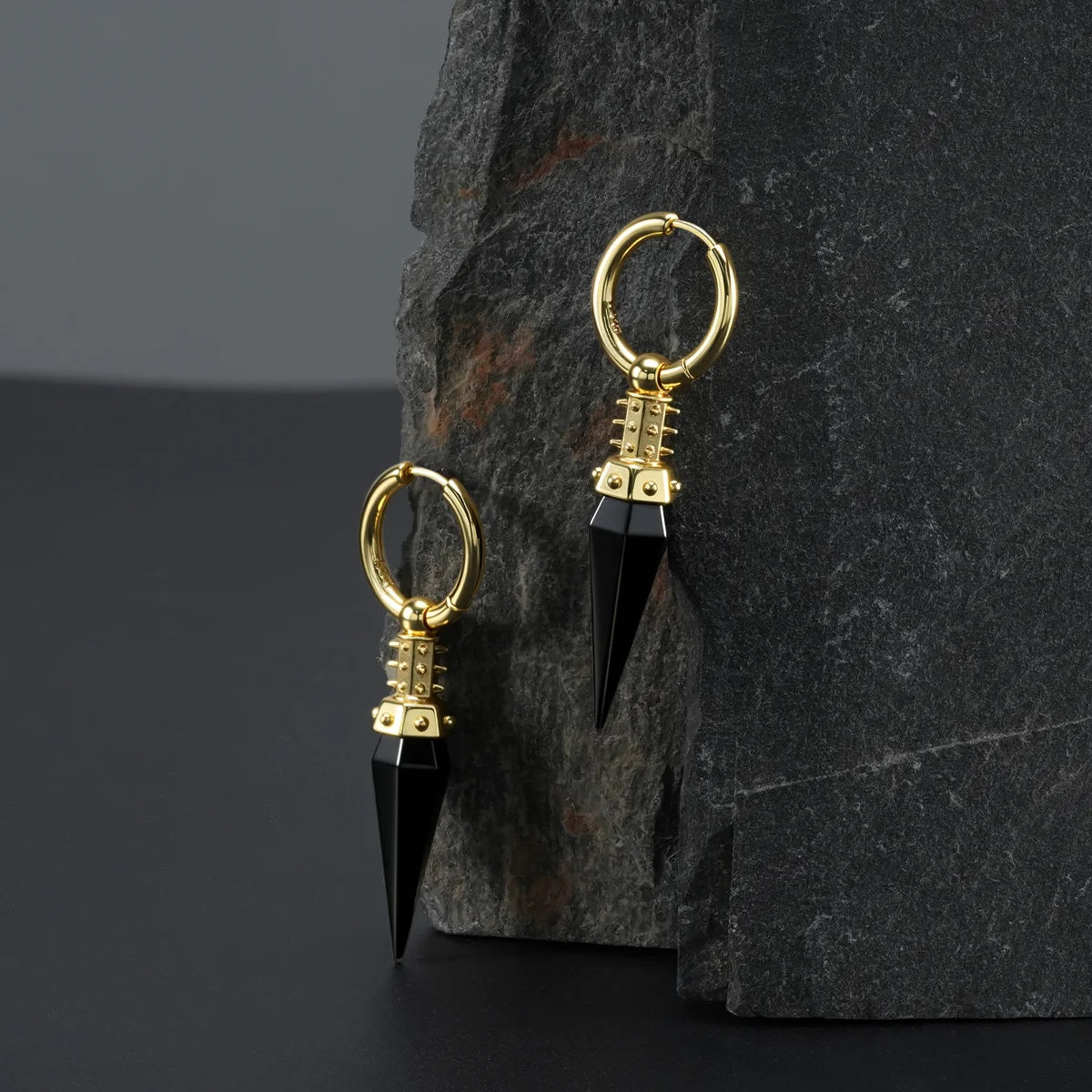 Gold Rivet Prism Earrings displayed on a dark stone surface, highlighting the black crystal spikes, rivet-like collar details, and polished hoops.