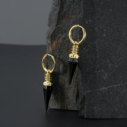 Gold Rivet Prism Earrings displayed on a dark stone surface, highlighting the black crystal spikes, rivet-like collar details, and polished hoops.
