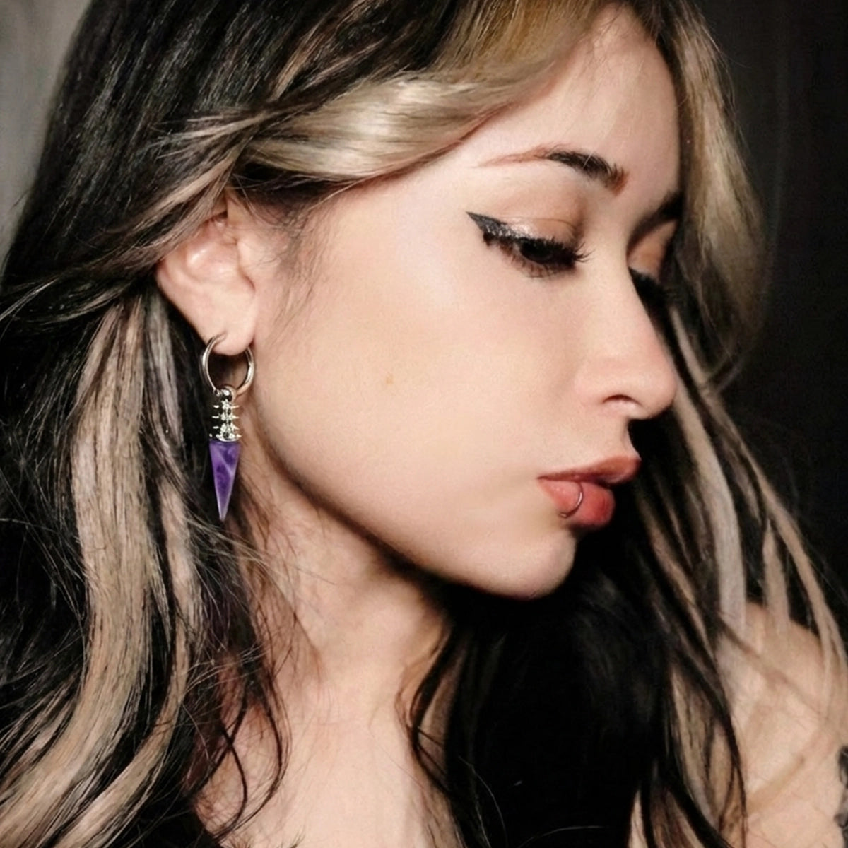 Model wearing the silver Rivet Prism Earrings with violet crystal spikes, polished hoops, and industrial gothic styling.