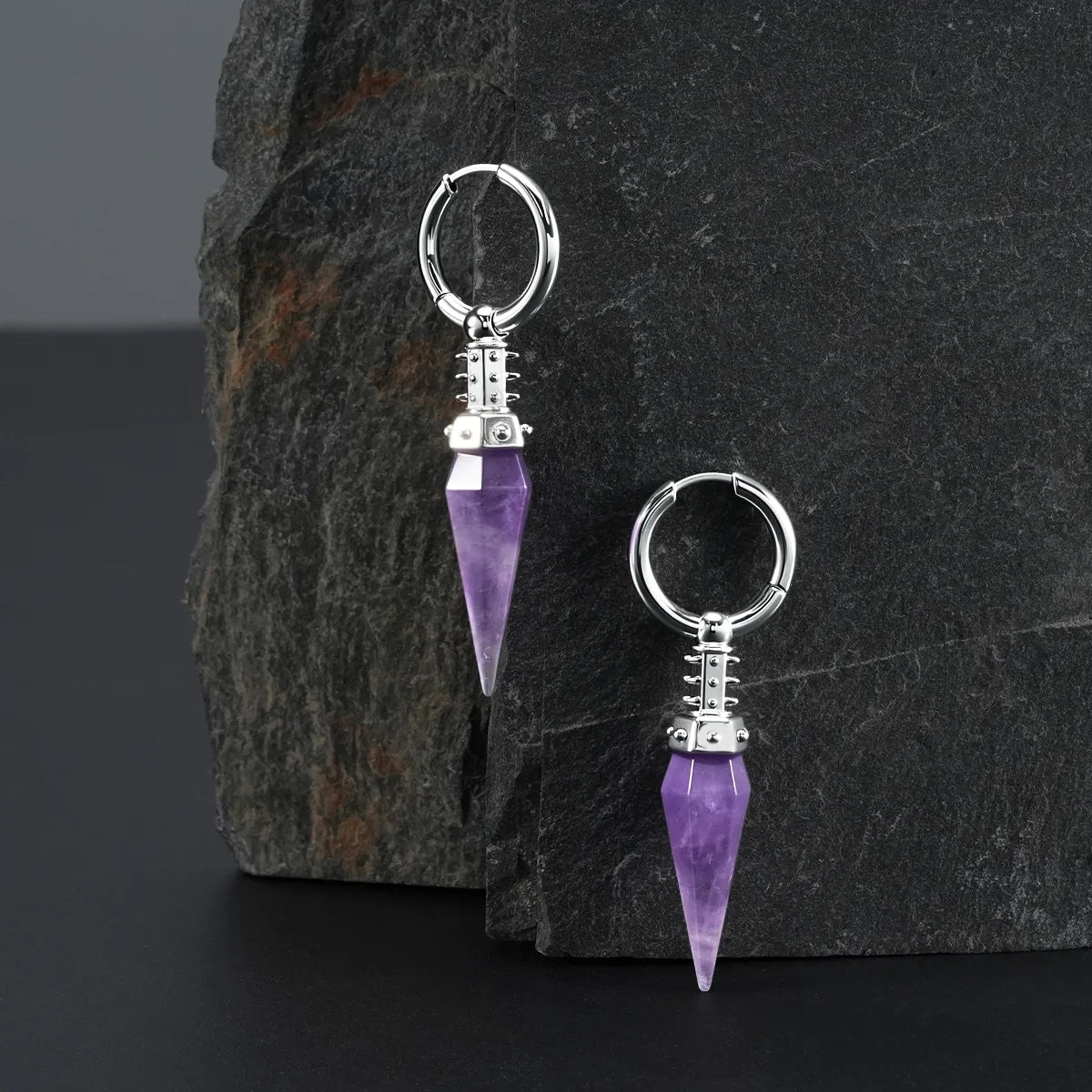 Silver Rivet Prism Earrings displayed on a dark stone surface, featuring violet crystal spikes, rivet-like collar details, and polished hoops.