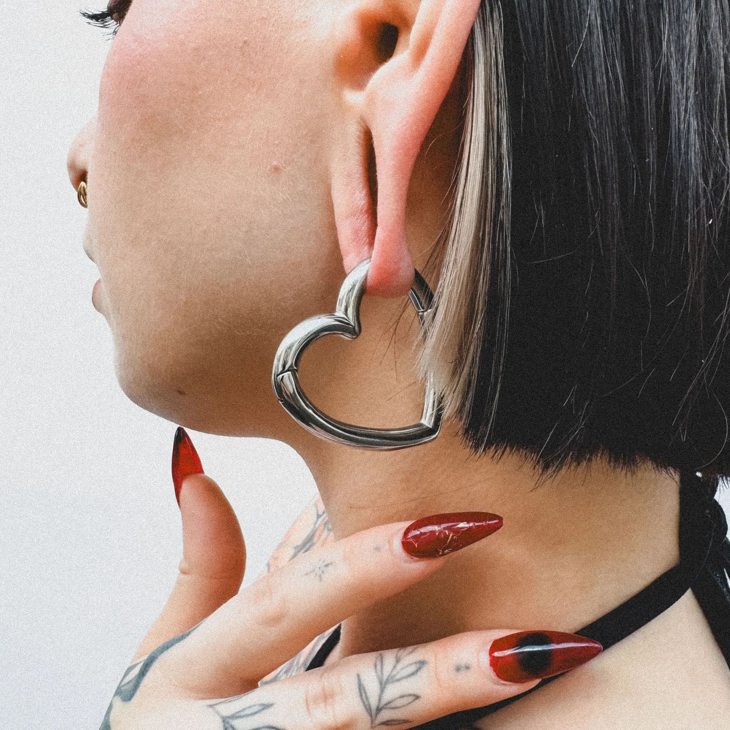 Silver-tone heart-shaped ear weight worn on a model's ear, close-up side profile view