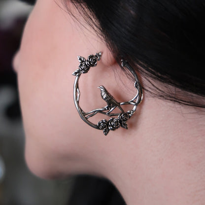 Close-up side view of a bird and rose hoop earring worn on a model's ear
