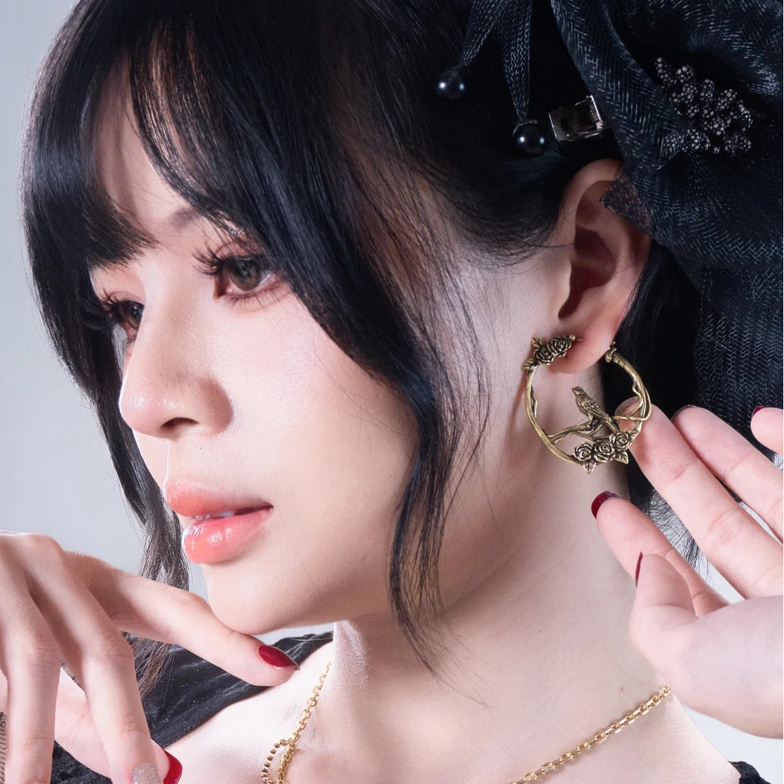 model wearing the rosebird hoop earrings in gold, shown in a side view with a bird and rose detailed hoop design