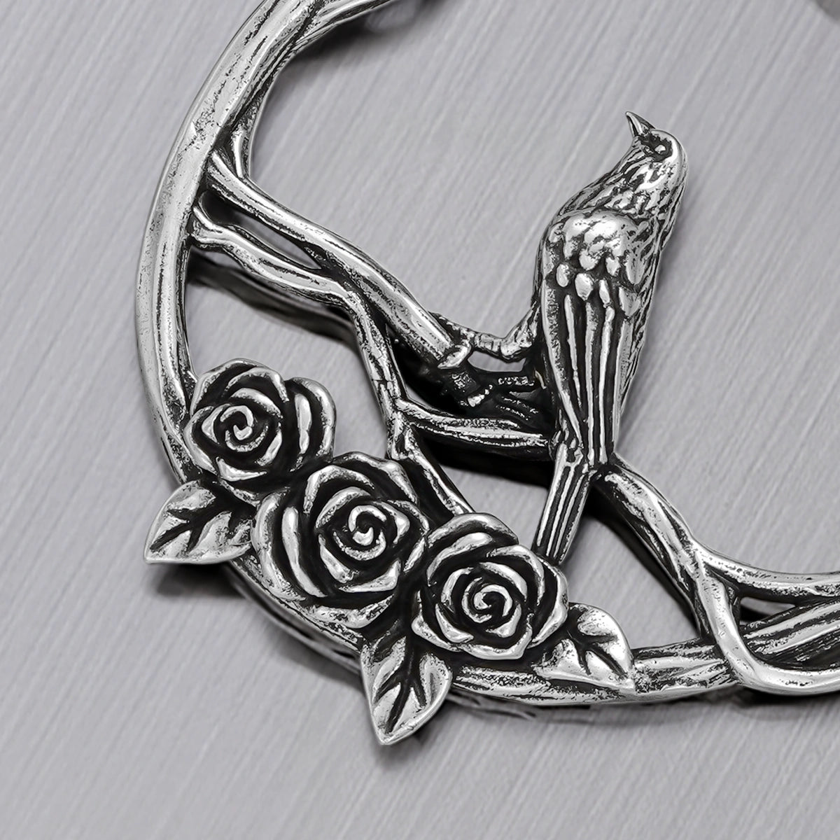 Close-up of silver Rosebird hoop earring with perched bird and sculpted roses