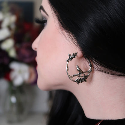 Dark-haired model wearing a silver-tone hoop earring featuring roses and a bird motif