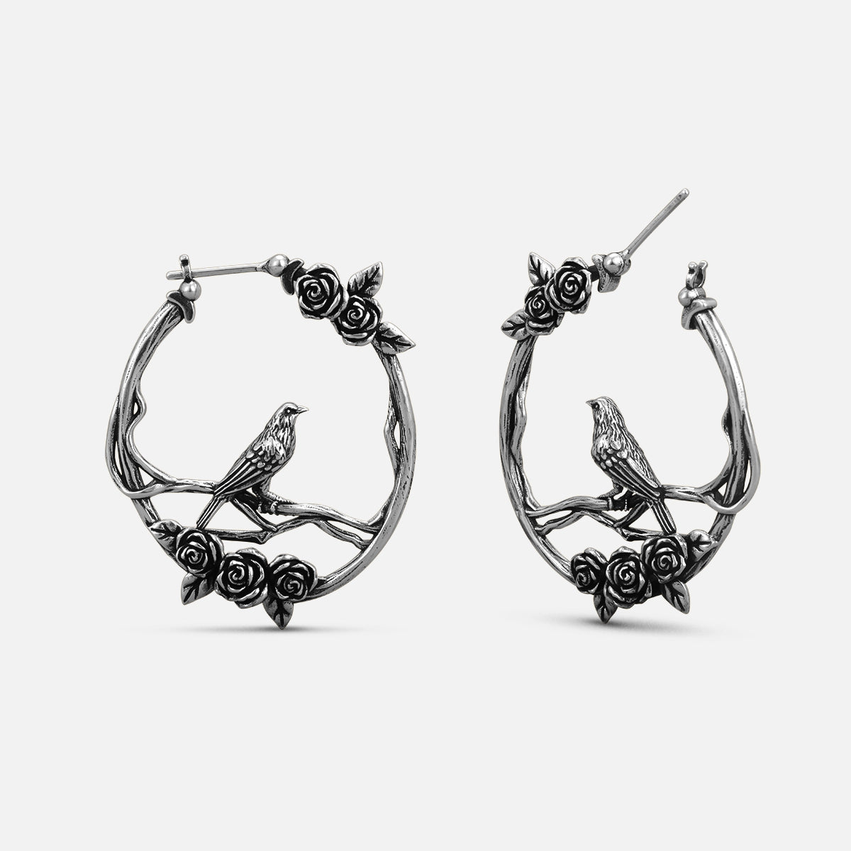 Pair of oxidized silver-tone hoop earrings with rose vine and perched bird design, front view
